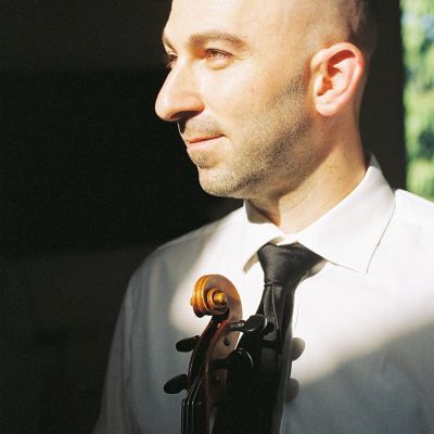 Daniel Pukach in a white shirt and tie. He holds a violin